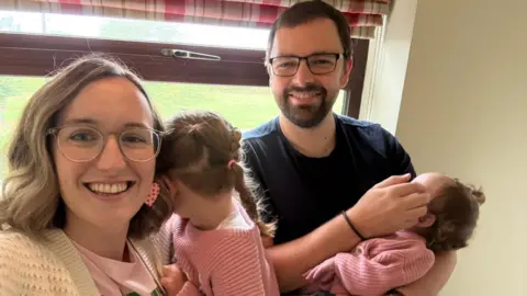 Supplied A smiling family made up of a woman, a man holding two little girls.
From right to left the