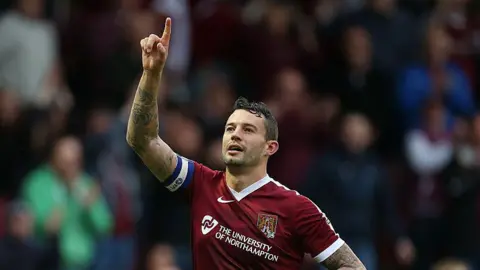 Getty Images A footballer wearing a maroon Northampton Town shirt raising his right arm in the air.