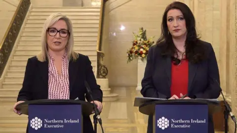 David Young/PA Wire Michelle O'Neill and Emma Little-Pengelly pictured giving a joint press conference to warn the public about Storm Éowyn last month.  They are both wearing dark suit jackets and coloured blouses and they are each standing behind lecterns in the Great Hall in Stormont.