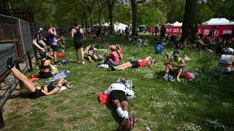 Getty Marathon participants rest and stretch in a park after completing the race, with trees and event facilities nearby.
