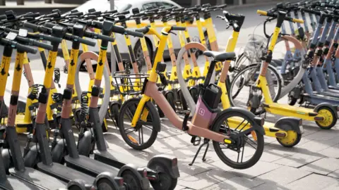A number of yellow and pink E-bikes lined up as they are charging. 