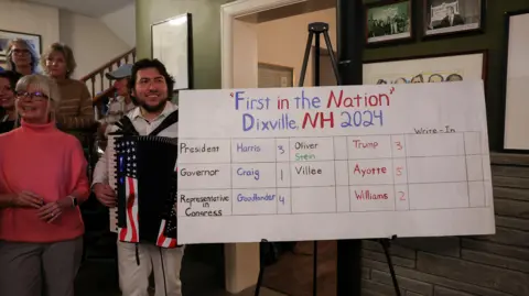 Reuters A crowd stands beside a whiteboard with the results of Dixville Notch's vote.