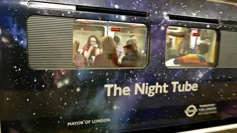 Getty Images London Underground train wrapped in a galaxy-themed design at a station platform, with passengers visible through the windows. Large white text on the train reads “The Night Tube,” alongside Transport for London and Mayor of London branding.