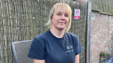 Louise Fewster/BBC Caroline Lane sitting outside in front of bamboo fence