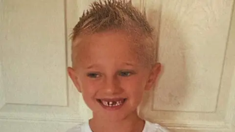 Family handout Freddie Farrow with his blond hair spiked up. He is standing in front of a door and smiling while wearing a white T-shirt.