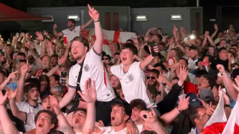 hundreds of football fans cheering happily inside a large room 