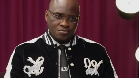 BBC Pastor Tobi Adegboyega wearing a black and white jumper with a Louis Vuitton tie. 