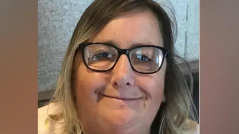 Family picture The image is a close-up, head-and-shoulders photograph of a person indoors. The person has medium-length hair that falls to around shoulder level, with darker tones near the top transitioning to lighter tones toward the ends. The hair is parted slightly to one side. The person is wearing rectangular, dark-framed glasses. 
