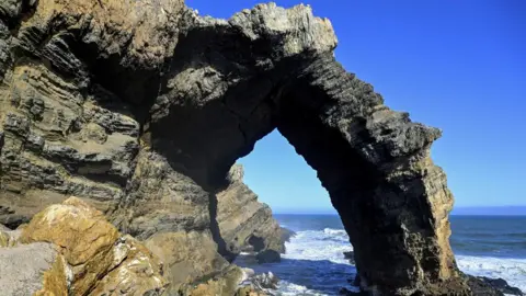 Getty Images Bogenfels arch - a natural rock formation. It is a 55m (180 ft) arch by Namibia's coast. Blue sea and sky are seen in the background.