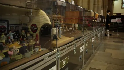 BBC A series of glass cabinets sit on a stone flagged floor. Inside the cabinets are scenes from World War Two. A London Underground station, with people sheltering, can be seen in the nearest cabinet.