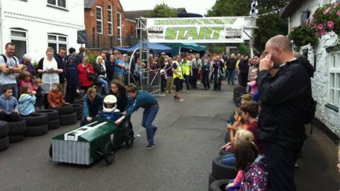 A team pushes a green soapbox whilst a crowd watches 