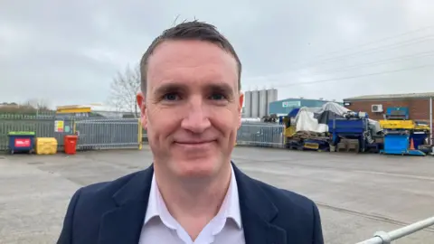 David Crew smiling at the camera on the forecourt of a business on a Somerset industrial estate