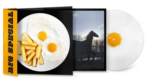 Tom Hicks/Alfie Hicks Artwork for Big Special's album National Average. On the album cover the band's name is in black letters on an orange background vertically on the left hand side. Next to it is a white plate of two fried eggs next to some chips. The egg yolks have been pixilated. An inner sleeve shows a black horse against a blue sky. An image of the vinyl disc is a fried egg. 