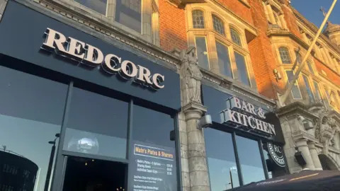 A bar with a Redcorc Bar & Kitchen sign at the top.