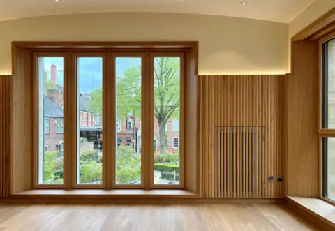 Ranjit Singh Chaggar A wood-panelled wall with a large window looking out on to a garden area