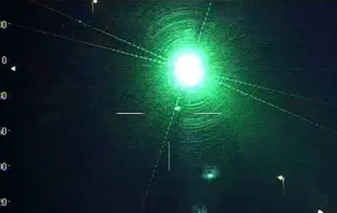 A blurred green laser light shining brightly on a dark background