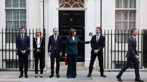 Reuters British Chancellor of the Exchequer Rachel Reeves holds the red budget box outside 11 Downing Street, as she stands with members of her team, in London, Britain, November 26, 2025.