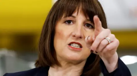 PA Media Rachel Reeves has dark brown hair cut into a bob with a fringe. She is wearing red lipstick, a black jacket and is pointing at the camera. She is wearing dark nail varnish and has two rings on her ring finger.