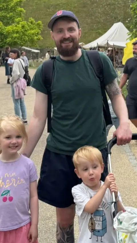 A man with a beard and a hat, in a green top and black shorts.