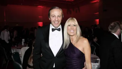 Press Eye A man in and woman in black tie and formal dress standing arm in arm smiling at the camera
