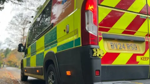 The rear side of an ambulance, parked on a road on an autumn day. 