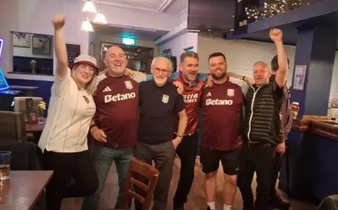 Punters at The Oak in Walmley who are wearing Villa home and away shirts have the fists aloft and are cheering their team's victory.
