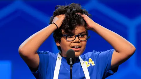 A child grips his hair with both hands as he stands on stage at the Scripps National Spelling Bee