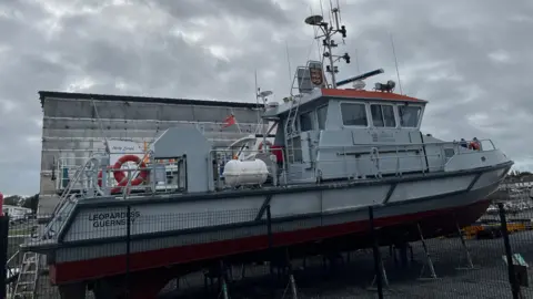 BBC The Leopardess - A grey boat on stilts behind a fence. 
