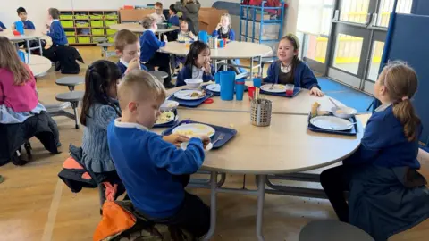 Children in uniform sat around tables eating their lunches from trays