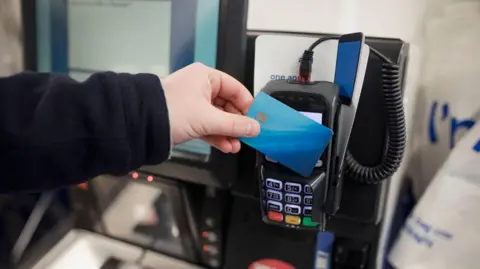 Getty Images Man presses a payment card to a reader at a self-service till in a supermarket.