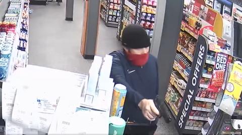 CCTV footage of a man covering his face in a service station pointing a fake gun at the cashier