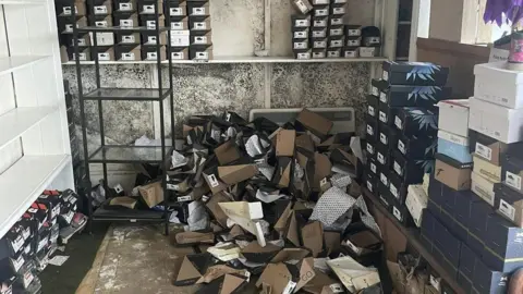 Dave Hammond A room full of boxes of shoes that have fallen over and large black mould patches on the wall.