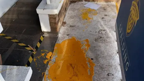 Spalding United FC Orange paint is spilt on a floor next to a blue Spalding United FC poster