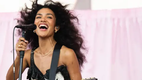 Getty Images Olivia Dean clasps a microphone while performing in concert