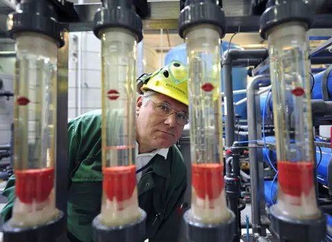Getty Images Refinery worker wearing yellow hard hat and green top observes four transparent glass tubes - archive picture