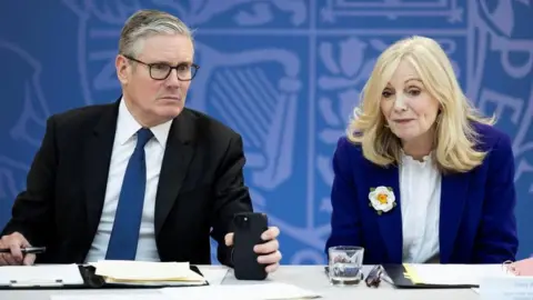 Sir Keir Starmer sits alongside Tracy Brabin at a desk, with a blue background. 