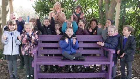 An excited boy sitting on a purple bench surrounded by other children and adults