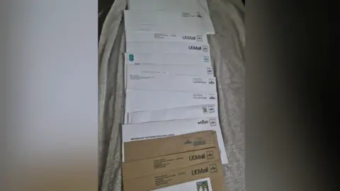 Handout A picture submitted by a contributor showing a number of letters that arrived in one delivery. In the photograph, three brown envelopes and several white envelopes from different companies are laid down in a column on a grey blanket. 