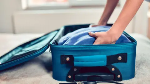 A stock image of a person placing a blue jumper into a blue suitcase.