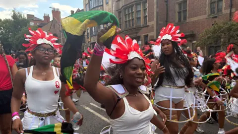 Three women at the front of the image, two carrying Jamaica flags