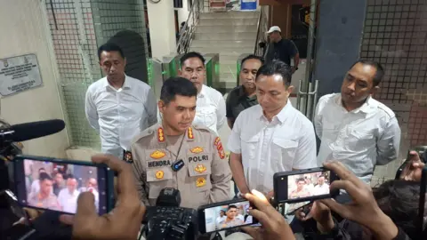 West Java Regional Police Representatives from Indonesia's West Java Regional Police addressing reporters outside the branch office. They are flanked by cameras and reporters filming on their mobile phones