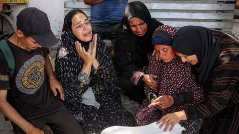Palestinians mourn a person killed as they waited for a convoy of aid lorries on the coastal road north-west of Gaza City, at al-Shifa hospital, northern Gaza (14 June 2025)