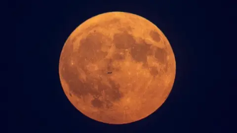 Getty Images An airplane flies in front of the Moon in Toronto.