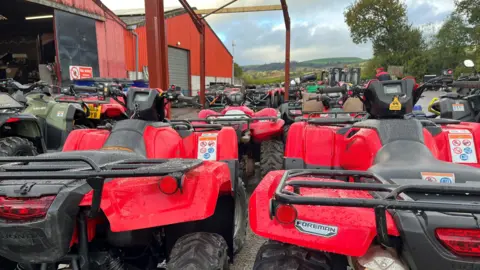 Dozens of red quad bikes in the outside area of a farm