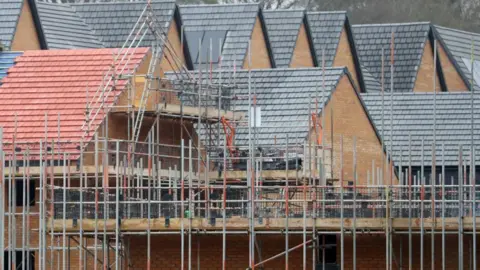 A construction site with mostly finished build residential buildings surrounded by scaffolding.