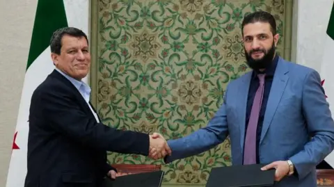 SDF commander Mazloum Abdi (L) shakes hands with interim Syrian President Ahmed al-Sharaa in Damascus on 10 March 2025