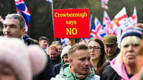 Getty Images A woman holding up a sign which says 'Crowborough says NO'. There are Union Jack and England flags in the background, and a crowfd of people. 