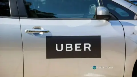 The outside of a silver vehicle with a black and white sign with the words "Uber" and "zero emission".