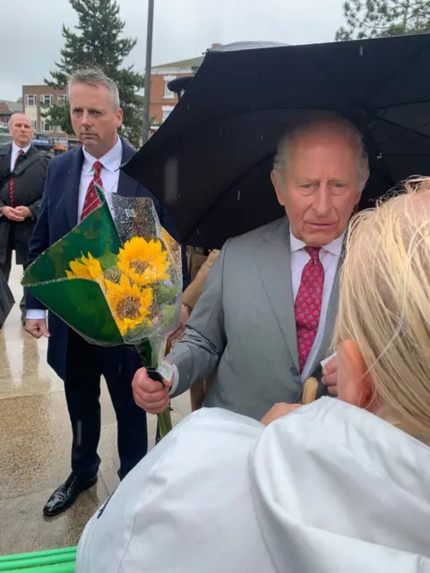 A woman presents King Charles with a bunch of yellow flowers during an impromptu walkabout in the town.