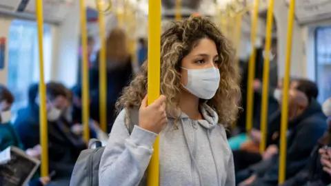 Getty Images Woman standing on a bus wearing a mask